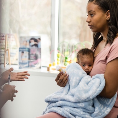 The serious new young adult mother holds her baby to her chest as she listens to the unrecognizable doctor describe possible side effects of a new medication.